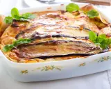 Parmigiana di melanzane napoletana recién horneada, dorada y burbujeante, decorada con hojas de albahaca fresca.