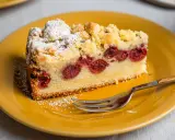 Ein saftiger Kirschkuchen aus der Springform, bestäubt mit Puderzucker und Streuseln, auf einem gelben Teller mit einer Gabel.