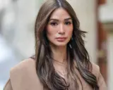 Mujer con cabello castaño largo y ondulado, viste un abrigo beige. Su maquillaje es sutil, un estilo "old money" que realza su belleza natural.