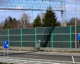 Znak drogowy informujący o odcinkowym pomiarze prędkości na tle ekranów akustycznych i drzew.