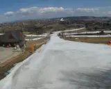Widok z kamery na stok w Bukowinie Tatrzańskiej. Śnieg na trasie, budynki i góry w tle.
