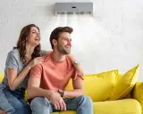 Couple souriant sur un canapé jaune, profitant de la brise fraîche d'un climatiseur moins de 50 db.