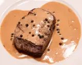Un steak tendre baignant dans une onctueuse sauce au poivre, parsemée de grains de poivre noir. Un délice pour les yeux et les papilles.