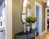 Élégant couloir maison avec miroir asymétrique, vases décoratifs, bouquet de fleurs jaunes et vue sur une salle de bain et une chambre.