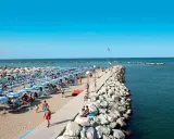 Spiaggia affollata a Gatteo Mare Cesenatico, con ombrelloni, lettini e persone che passeggiano sul molo.