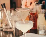 Ile napojów na wesele 80 osób? Barman przygotowuje drinka, w tle butelki z alkoholami i syropami.