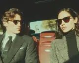 Coppia elegante in auto, lui con completo gessato e cravatta, lei con blazer a quadri. Un'idea per un outfit matrimonio inverno pantaloni chic.