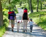 Familia con mochilas camina por un sendero boscoso, ideal para rutas para hacer con niños.