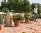 Mujer riega flores en macetas en una terraza, mostrando diferentes tipos de riego para mantenerlas sanas y vibrantes.