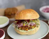 Wegański burger z kiełkami, czerwoną cebulą i sosem na talerzu.