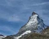 Majestatyczny polski Matterhorn, pokryty śniegiem, góruje nad krajobrazem. Na błękitnym niebie, wśród chmur, szybujący paralotniarz.
