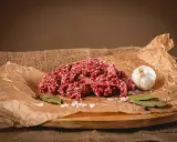 Surowe mielone mięso, idealne na soczyste burgery. Obok czosnek, liście laurowe i sól.