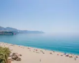 Sonniger malaga strand mit vielen Menschen, die sich unter bunten Sonnenschirmen entspannen. Das türkisfarbene Meer lädt zum Baden ein.