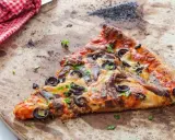 Une part de pizza aux anchois et olives sur une pierre réfractaire, prête pour un nettoyage.