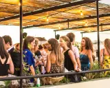 Menschen genießen den Abend auf einer Dachterrasse in einem **bar lissabon**. Unter einem Strohdach mit Lichterketten unterhalten sie sich bei Getränken.