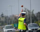 Policjant kieruje ruchem, podnosząc znak stop. W tle widać samochody i słupy oświetleniowe, sugerujące podwyższone **stopnie alarmowe**.
