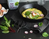 Jak zrobić dobry omlet? Oto inspiracja: puszysty omlet z rzodkiewką, ogórkiem i ziołami na czarnej desce.