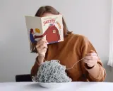 Dziewczyna czyta książkę o swetrach, jedząc spaghetti z włóczki. Jak znaleźć początek włóczki?