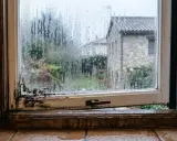 Marco de ventana con moho y gotas de agua. La humedad se acumula en el cristal, empañándolo y dificultando la vista del exterior.