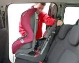 Mężczyzna montuje fotelik samochodowy. Sprawdź, jak sprawdzić, czy samochód ma isofix, patrząc na zaczepy fotelika.