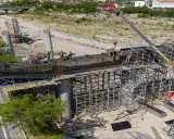 Obreros trabajan en la construcción de puentes de acero, con grúas y andamios rodeando las estructuras.