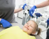 Uśmiechnięta dziewczynka na fotelu dentystycznym, przygotowywana do zabiegu z użyciem sedacji wziewnej.