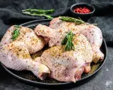 Quatre cuisses de poulet crues, assaisonnées et garnies de romarin, prêtes pour une marinade poulet savoureuse.