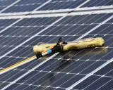 Reinigung von Solaranlagen mit einem Teleskopwischer. Gelber Wischerkopf auf dunklen Solarzellen.