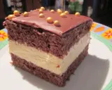 Pyszne milky way ciasto z czekoladowym blatem i kremowym nadzieniem, ozdobione złotymi kuleczkami.