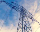 Wysoki słup energetyczny z liniami przesyłowymi na tle błękitnego nieba z chmurami. Linie te, niczym niewidzialne ley lines, niosą energię.