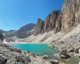 Il **lago di Antermoia**, incastonato tra imponenti pareti rocciose, brilla di un turchese intenso sotto un cielo azzurro.