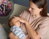 Zmartwiona mama sprawdza gorączkę u śpiącego niemowlaka. Obok wirus RSV, który może powodować groźne objawy u dzieci.