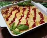 Pyszne, zapieczone fit lasagne w białym naczyniu, polane ketchupem i ozdobione listkami bazylii.