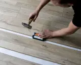 Mann verlegt Laminat mit Hammer und Schlagklotz. Die neuen Dielen werden präzise zusammengefügt.
