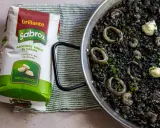 Arroz negro con calamares y gambas en paellera, junto a un paquete de arroz redondo Sabroz.