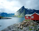 Två röda stugor vid en sjö med dramatiska berg i bakgrunden. Perfekt för att vandra i Norge.