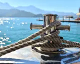 Corde épaisse enroulée autour d'une bitte d'amarrage en acier inoxydable. Le soleil brille sur l'eau bleue. Cela illustre comment fonctionne une ancre de bateau.