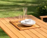 Vacker teakmöbel som behöver behandlas för att behålla sin lyster. Tallrikar, skålar och glas står redo för en utomhusmåltid.