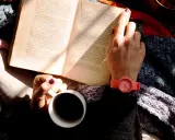 Kobieta z kawą i książką po angielsku B2, otulona ciepłym kocem, cieszy się chwilą relaksu.