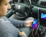 Mężczyzna w samochodzie pokazuje, jak połączyć telefon z autem za pomocą kabla i aplikacji Weblink. Na ekranie radia widoczne są ikony aplikacji.