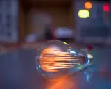 Żarówka LED 8 watt ile to wat? Widoczna żarówka z rozżarzonym żarnikiem, w tle kolorowe światła.