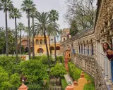 Frau blickt lächelnd aus einem Säulengang auf üppige Gärten mit Palmen. Ein versteckter Blick auf Sevilla, der Lust auf mehr macht. #sevilla #geheimtipps