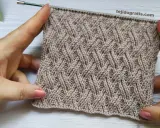 Manos sostienen un tejido cruzado de lana beige con un patrón de rombos entrelazados.