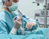 Lekarz w masce i rękawiczkach przygotowuje się do zabiegu, trzymając urządzenie do biopsji. Czy biopsja prostaty może uaktywnić raka?