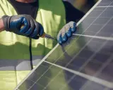 Mains nues, gants bleus et jaunes, tournevis en action pour la réparation d'un panneau solaire.
