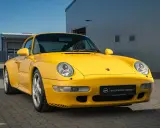 Gelber Porsche 993 vor einem modernen Gebäude. Die Wertentwicklung dieses Klassikers ist bemerkenswert.