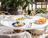 Delicioso brunch con niños en Madrid. Mesa con varios platos, copas de vino blanco y sillas blancas.