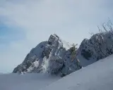 Masyw górski w Tatrach Zachodnich, pokryty śniegiem, z krzyżem na szczycie. W dole morze chmur.