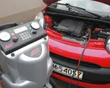 Urządzenie do serwisu klimatyzacji podłączone do czerwonego samochodu. Dowiedz się, ile kosztuje nabicie klimatyzacji.