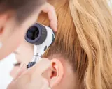 Un dermatologo esamina il cuoio capelluto con un dermatoscopio, eseguendo un pull test per valutare la caduta dei capelli.